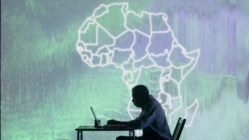 A man sits in front of an LED wall using a laptop