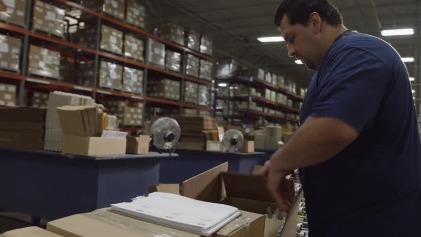 A man is picking items from boxes on a conveyor line in a warehouse