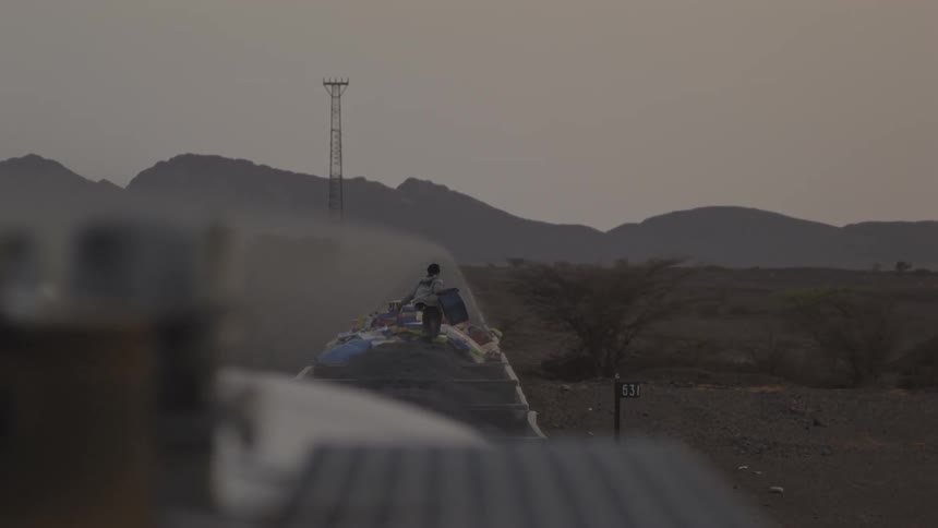 A person carries a box along the top of a moving rail car