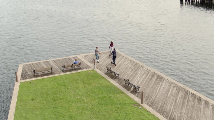 People riding kick scooters in an area next to some water in a city
