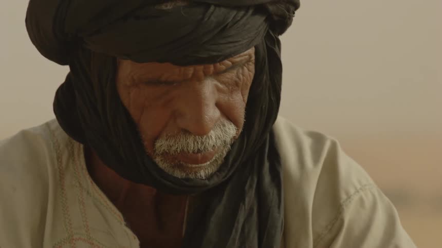 A old bedouin man is sitting outside in the desert making tea during the day