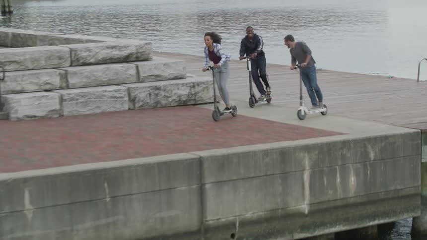 Friends ride scooters on a pier