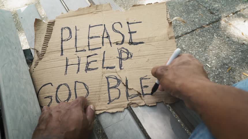 A man is writing a cardboard sign in marker