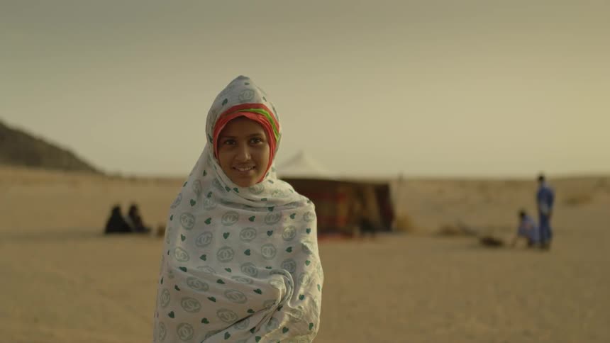 A young girl stands huddled in a blanket in the desert
