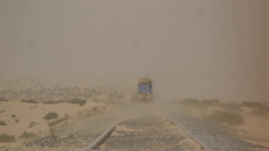 A truck is driving down a dusty desert road