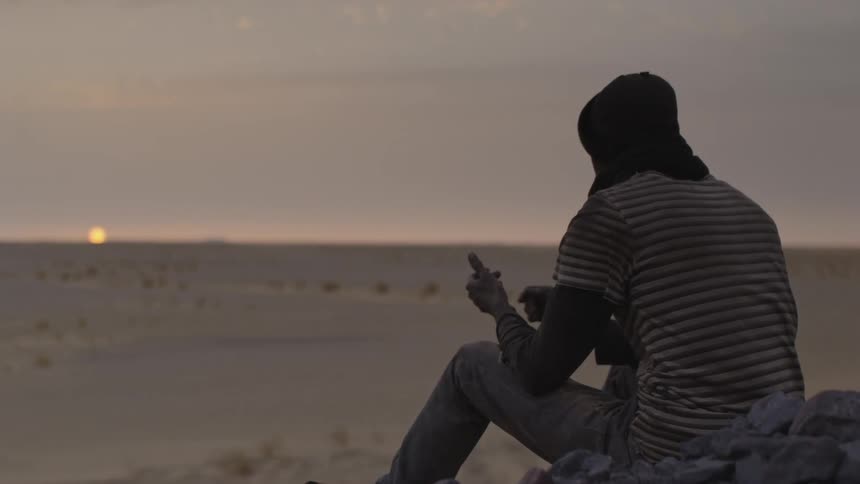A man riding a train through the desert at sunset