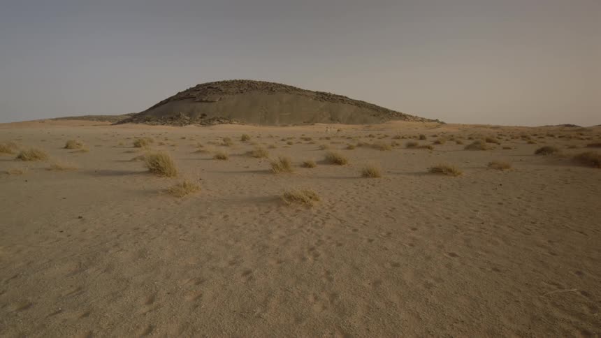 The wide open desert has a small hill in it