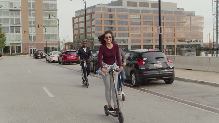 Three people riding scooters down the street