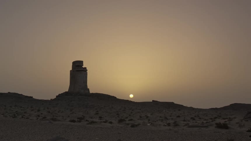 A broken building in a desert at sunset