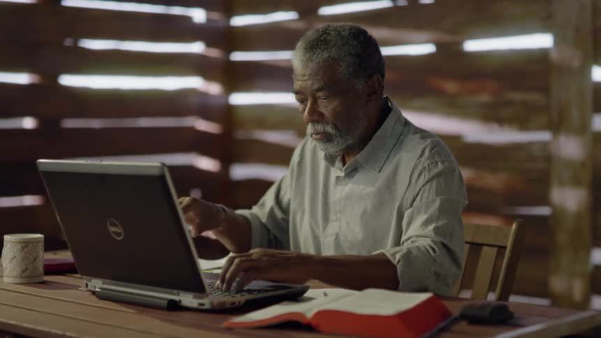 A man is sitting down using his laptop