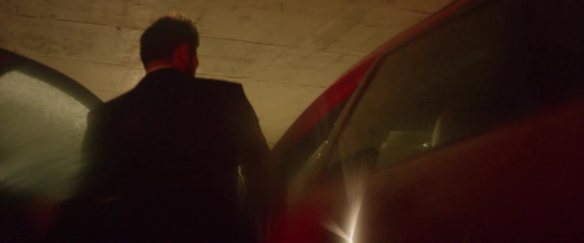 A man gets into a red car in a parking garage