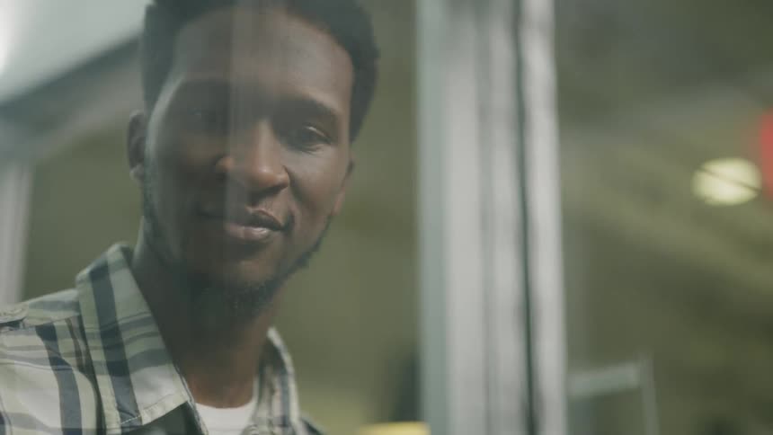 A man is smiling as he writes on a glass board in an office