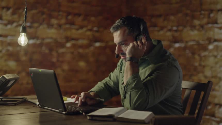 Man wearing headset talks while working on computer