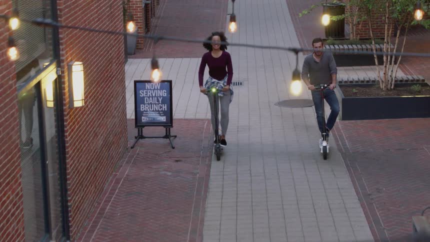 Two people smile while riding scooters