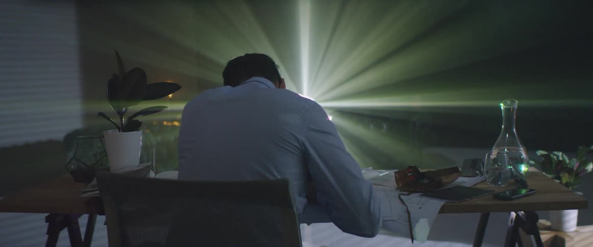 A man sits at a desk as a projector flashes images behind him