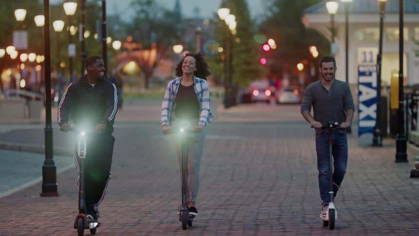 Friends ride scooters in a city at dusk