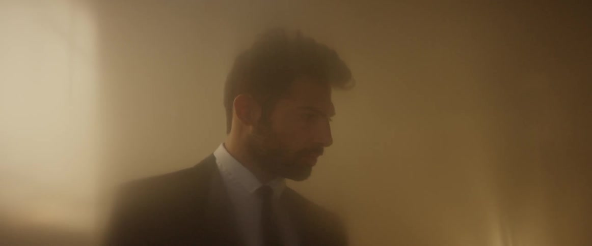 A man in a suit looks down as light comes in from behind him