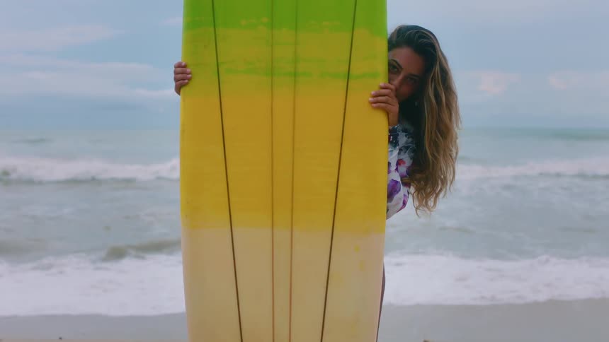 Woman holds a surfboard on a beach at sunset