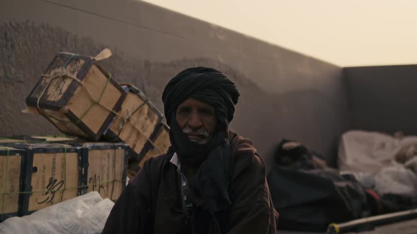 An elderly arab man is sitting outside on a dusty day