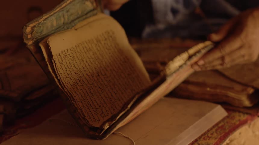 A man picks up an old book from a pile and then leafs through it