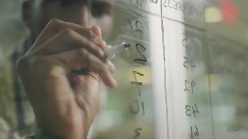 Man doing math on a glass pane using a marker indoors