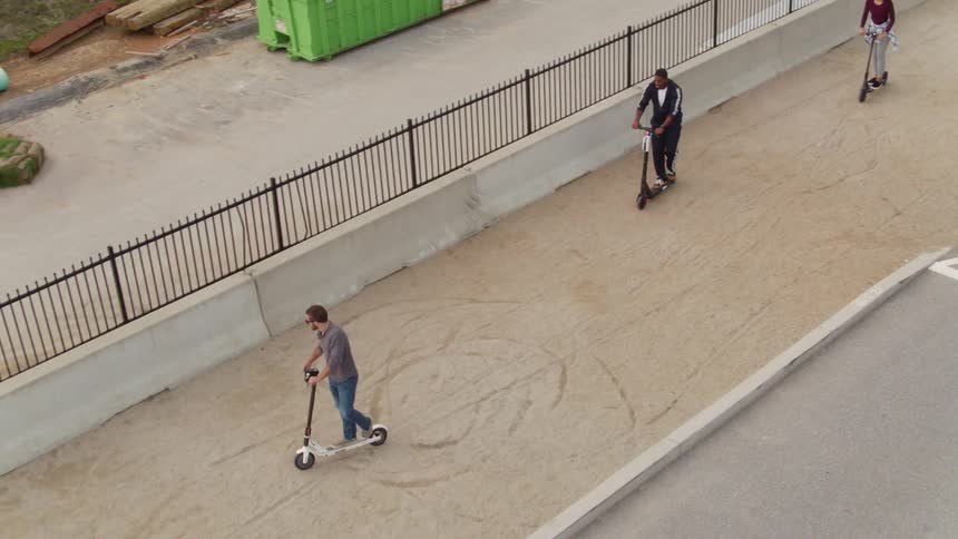 Friends ride scooters on a sidewalk above a construction site