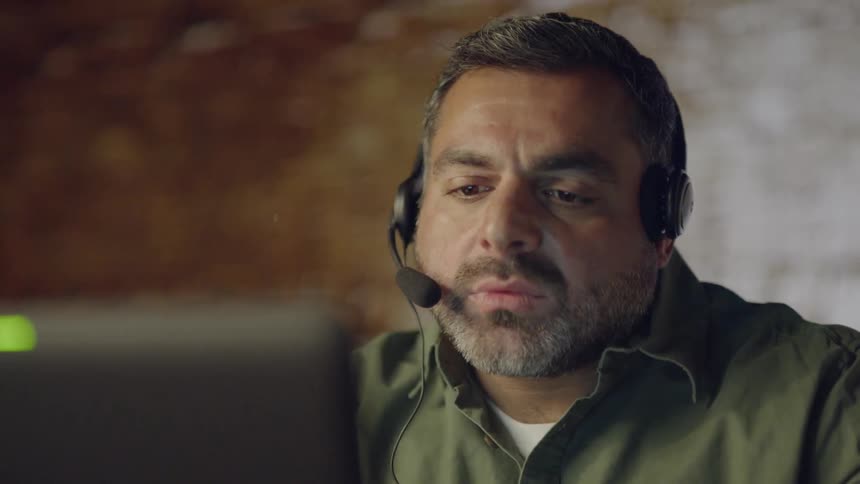 A man wearing a headset works on a computer