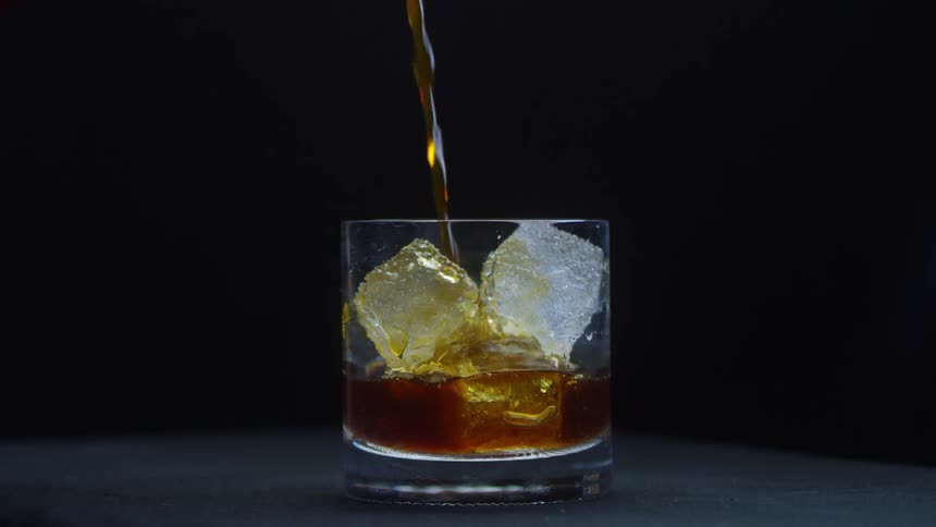 Whiskey is poured over ice in a glass