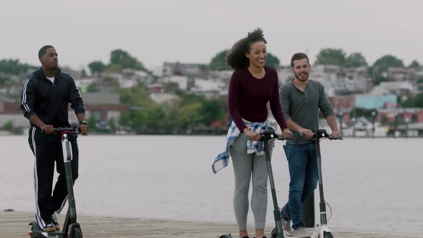 Three people are riding scooters by the waters edge