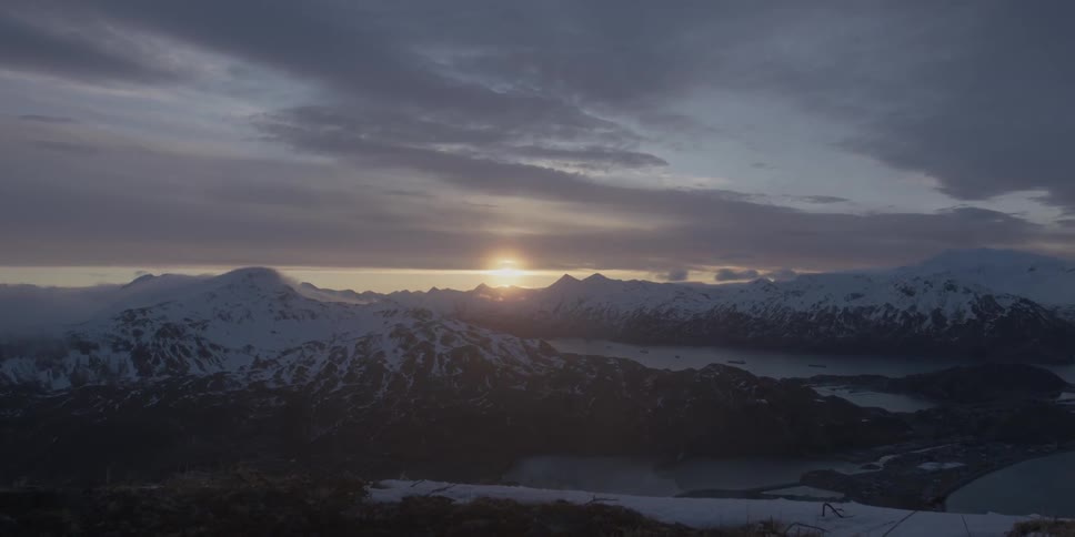 Sun setting behind snowy mountains on a cloudy evening