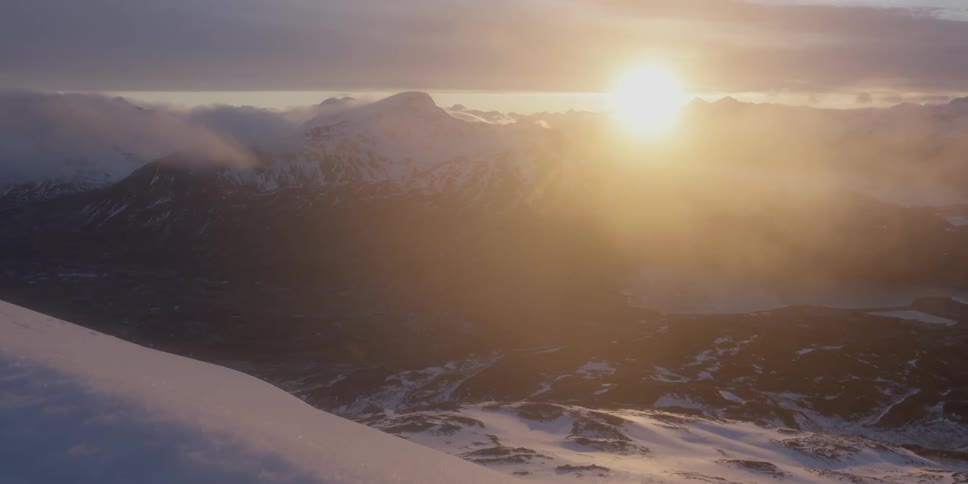 The sun is rising over a snow-covered mountain range