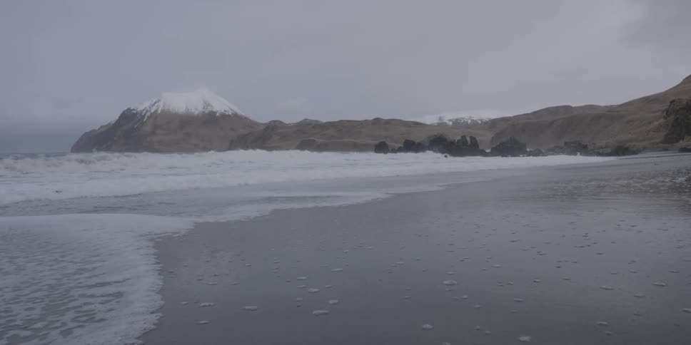Water coming ashore with snow capped mountains in the distance