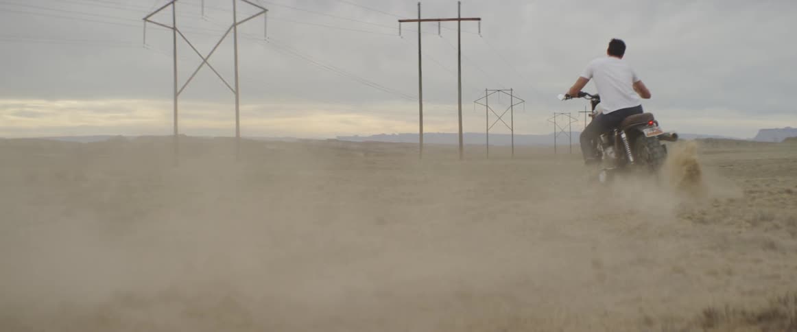 Man churns up dust while riding a motorcycle across a rural field
