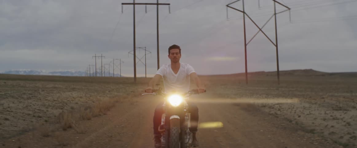 A man rides a motorcycle on a dirt road under power lines
