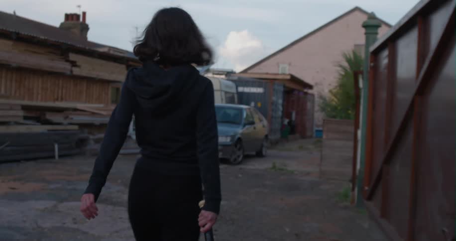 A woman walks down the lot with a baseball bat and smashes a car