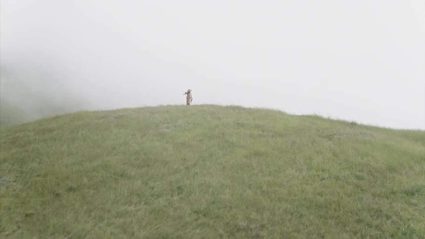 Man hikes on grassy field while carrying skis