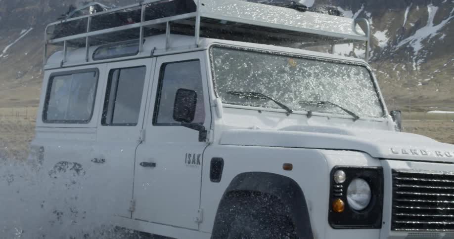 A land rover splashes through a shallow stream