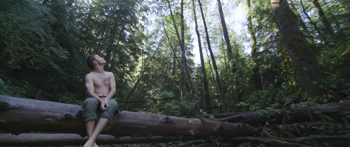 A man sits on a fell tree in the woods