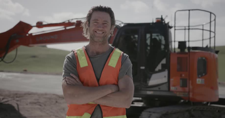 A construction worker smiles in front of machinery