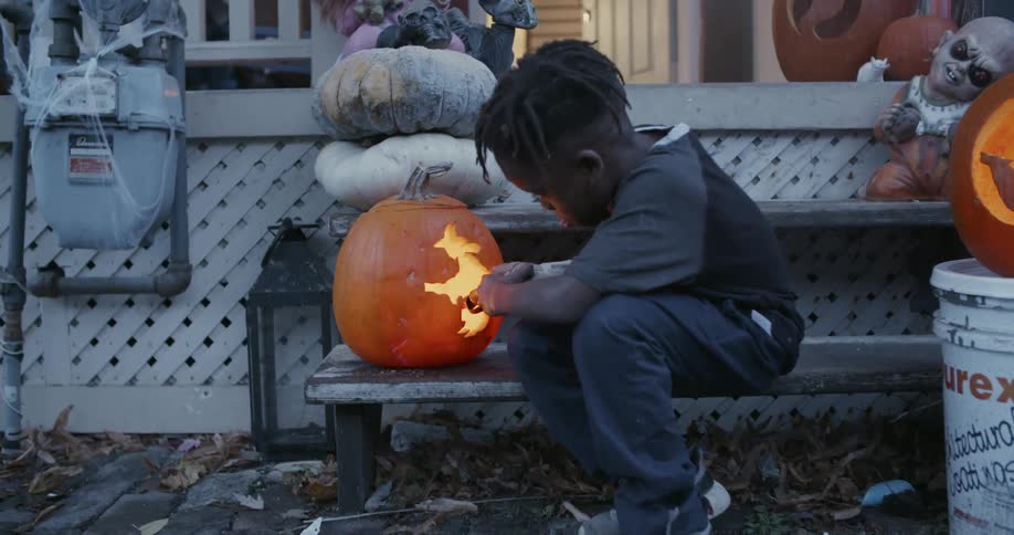 A child is on the porch carving a pumpkin