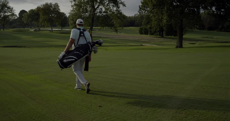 A man walks on the green carrying his golf bag