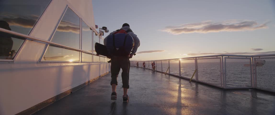 A skateboarder walks on the deck of a ship at sea