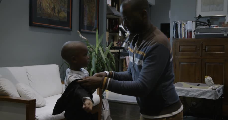 A man helps a child put on his shirt in the living room