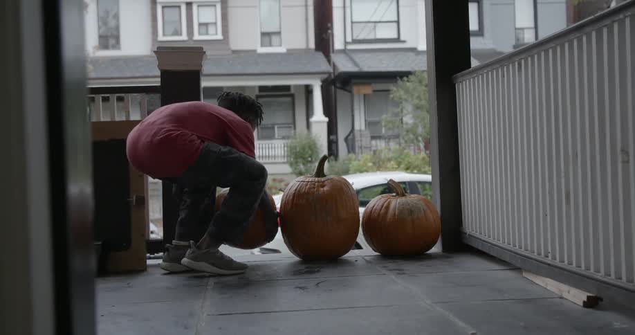 A young boy places a carved pumpkin by the front steps
