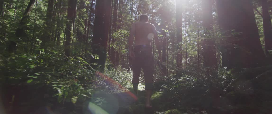 A man walks barefoot through the forest carrying his shoes