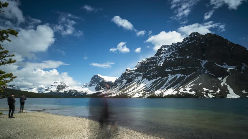 People walking on the Bow Lake shore near snow covered Canadian Rockies