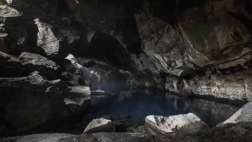 Sunlight shines through the rocks to the water and cavern below