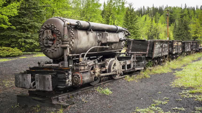 A derelict steam train is sitting idle on tracks in a forest in Bankhead Ghost Town in Banff