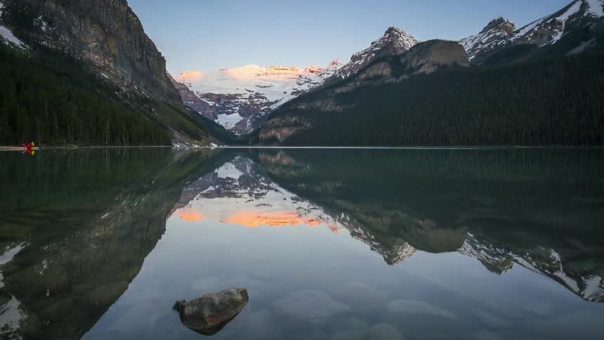 A perfect reflection of a sunrise coming out from behind scenic mountains over Lake Louise in Banff