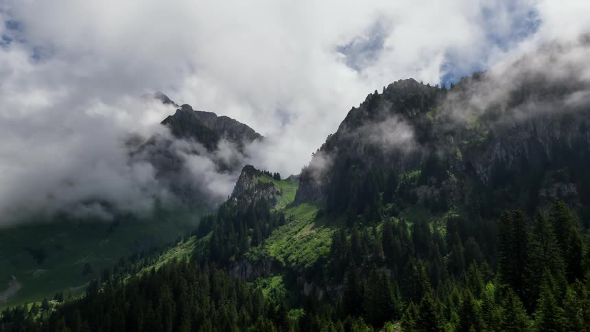 Clouds billowing over tree covered mountains
